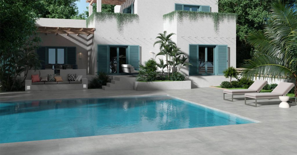 Piscine bordée de dalles grises, transats et maison blanche