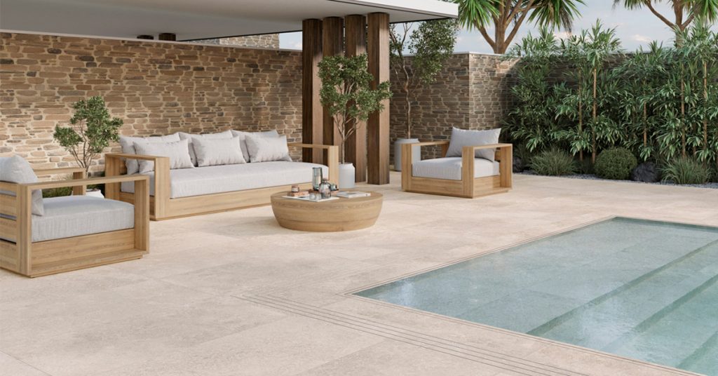Terrasse carrelée beige, canapé et fauteuil en bois, piscine rectangulaire