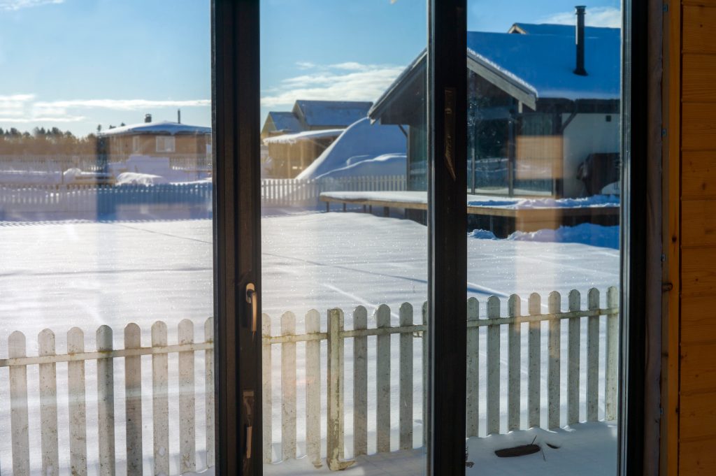 Barrière blanche à piquets dans la neige vue depuis la baie vitrée
