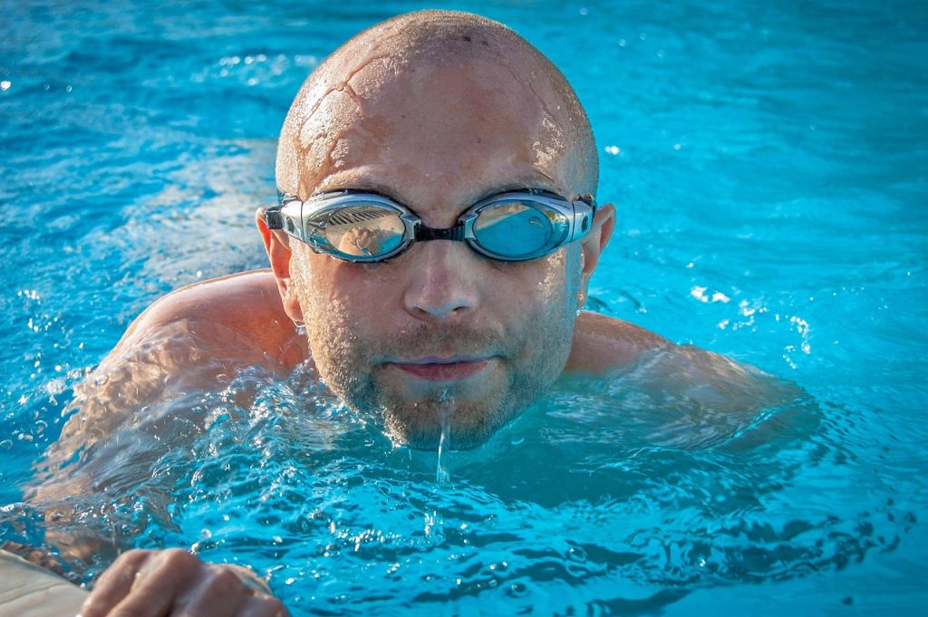 Homme nageant avec lunettes dans piscine bleue et limpide