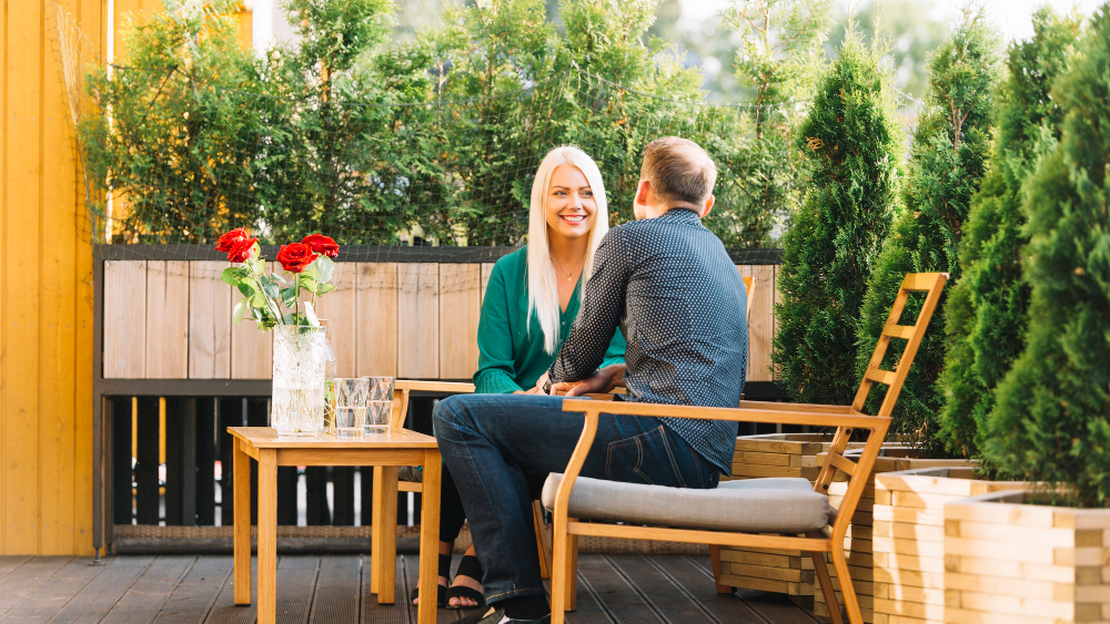 Couple sur fauteuils en bois, table basse, jardinières, salon de jardin